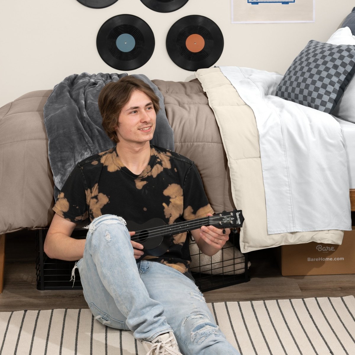 Person sitting on a bed holding a guitar in a bedroom setting with vinyl records on the wall.