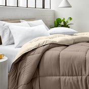 Bed with comforter and white pillows in a bright bedroom setting.