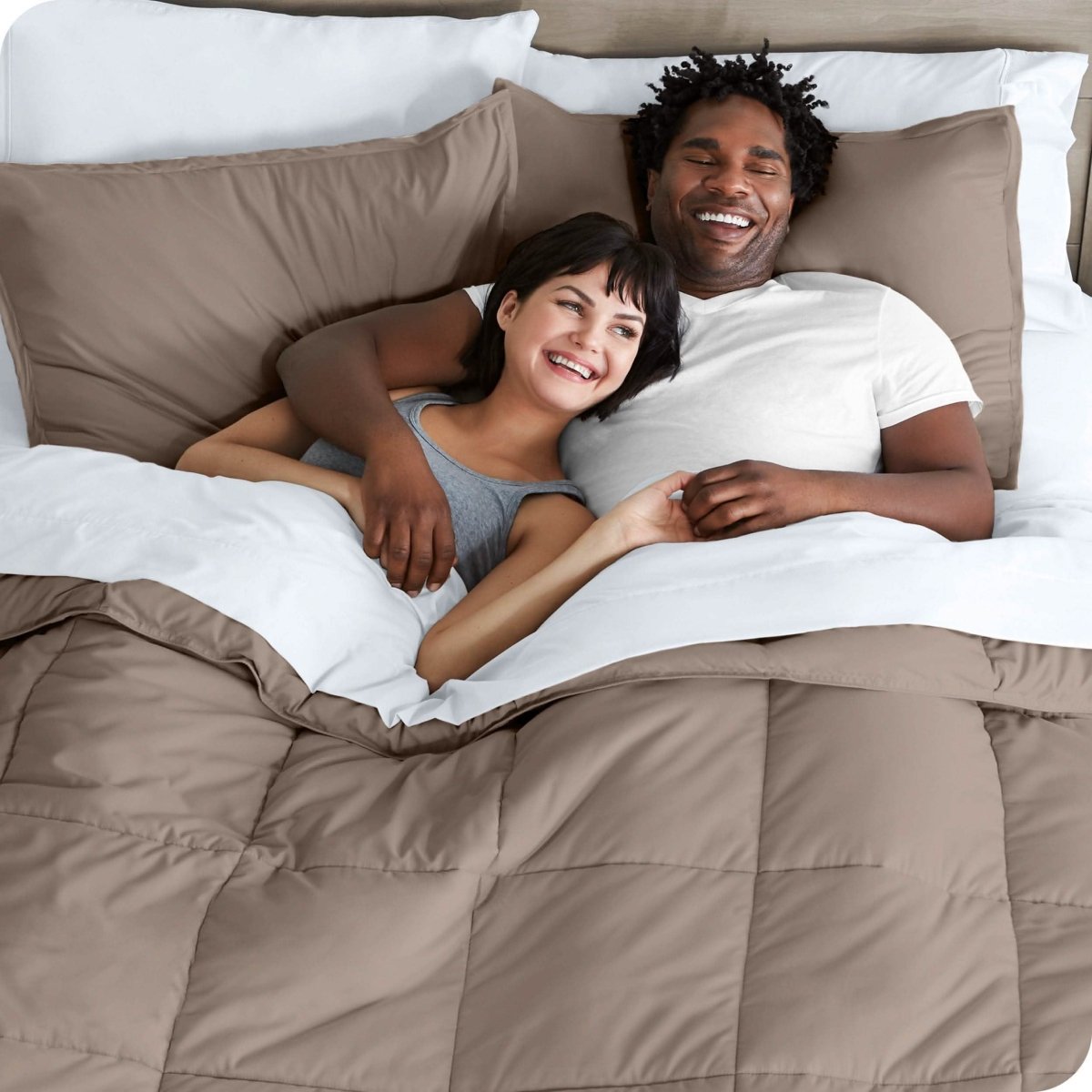 A couple is lying in bed with a comforter and sheets over them