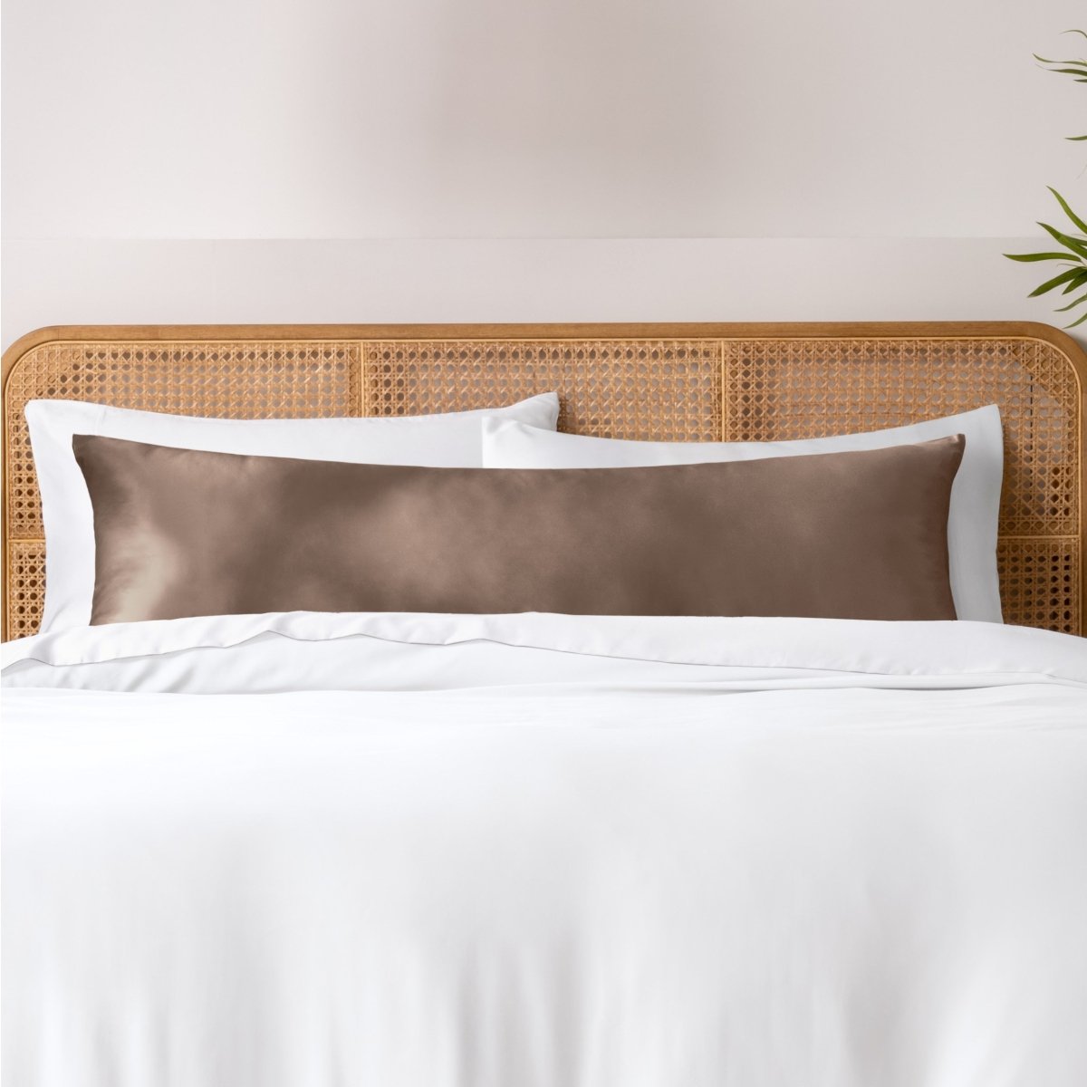 Pillows, sheets and a duvet cover on a bed with a wicker headboard and light gray bedding.