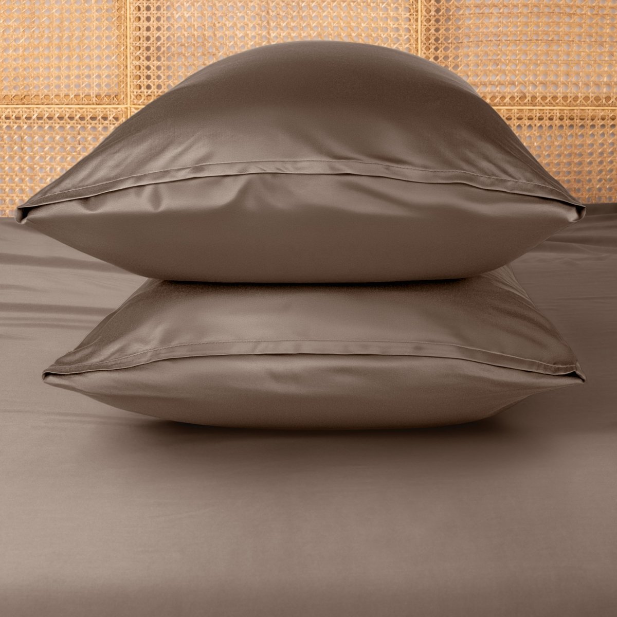 Two taupe pillows stacked on a bed with a woven headboard.