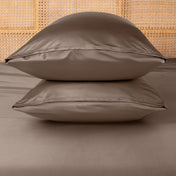 Two taupe pillows stacked on a bed with a woven headboard.