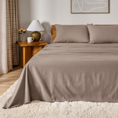 A bed dressed in flannel sheet set in a bedroom with a wooden headboard, bedside table and lamp
