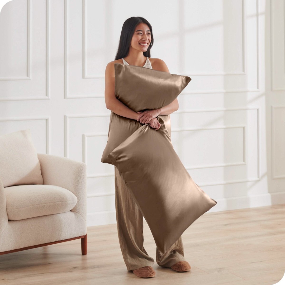 A woman standing while holding pillows with silk pillowcases on them