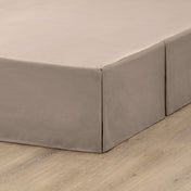 The corner of a box spring with a pleated bed skirt on it