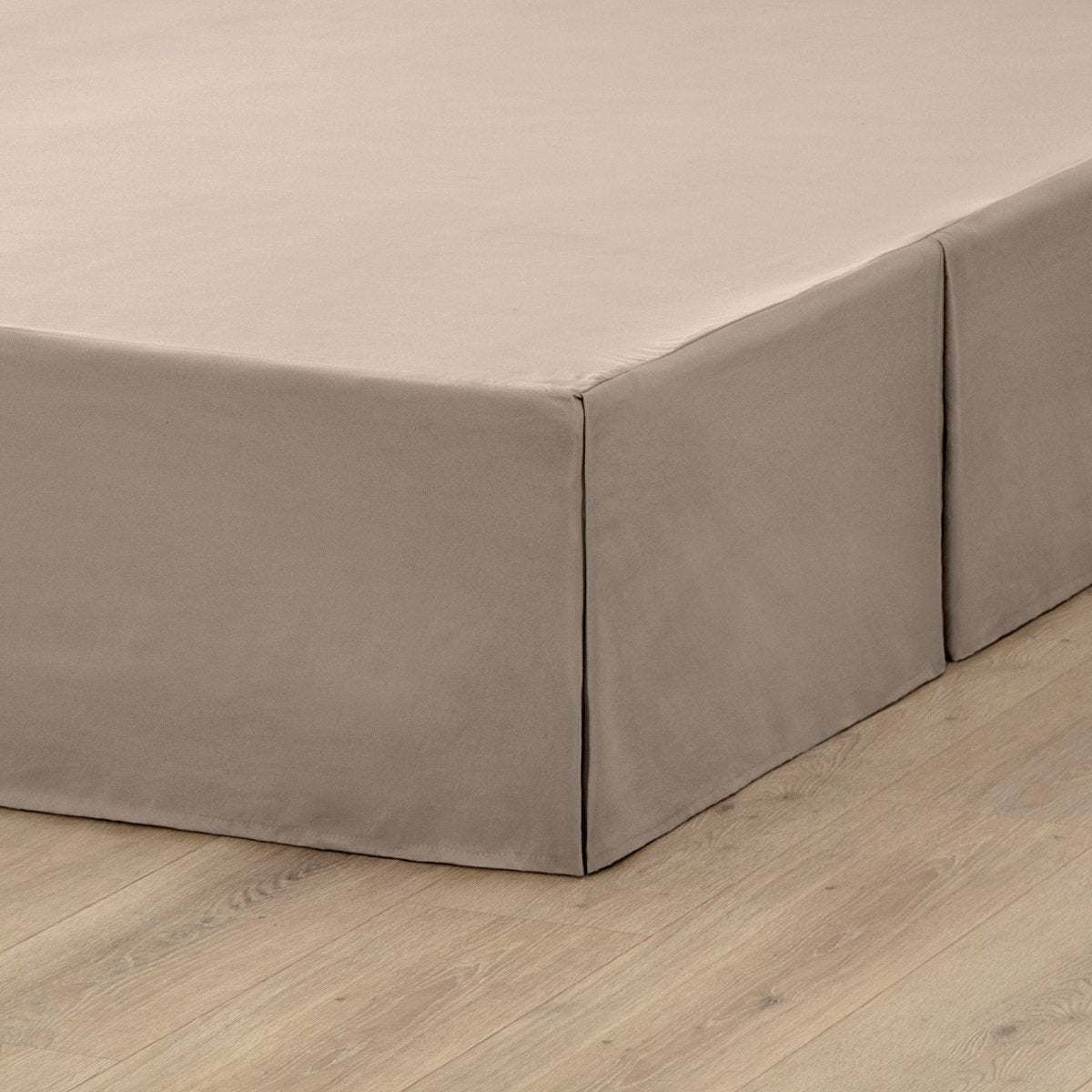 The corner of a box spring with a pleated bed skirt on it