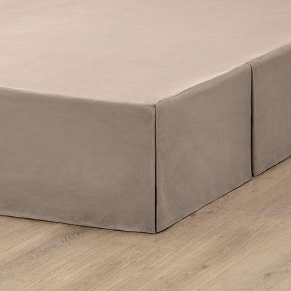 The corner of a box spring with a pleated bed skirt on it