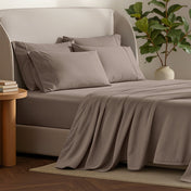 Bed sheets and pillows on a bed with a plant and side table in the background.
