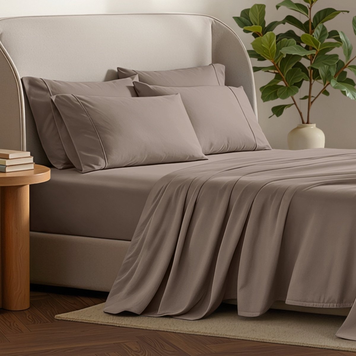Bed sheets and pillows on a bed with a plant and side table in the background.