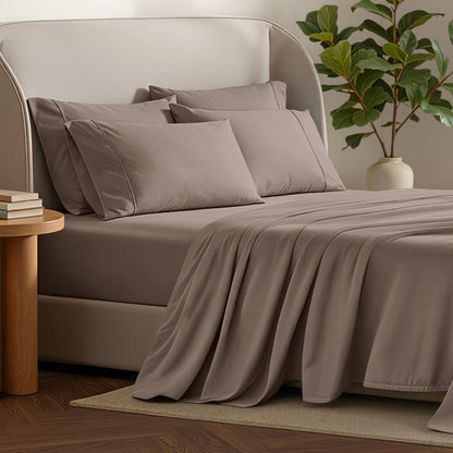 Bed sheets and pillows on a bed with a plant and side table in the background.
