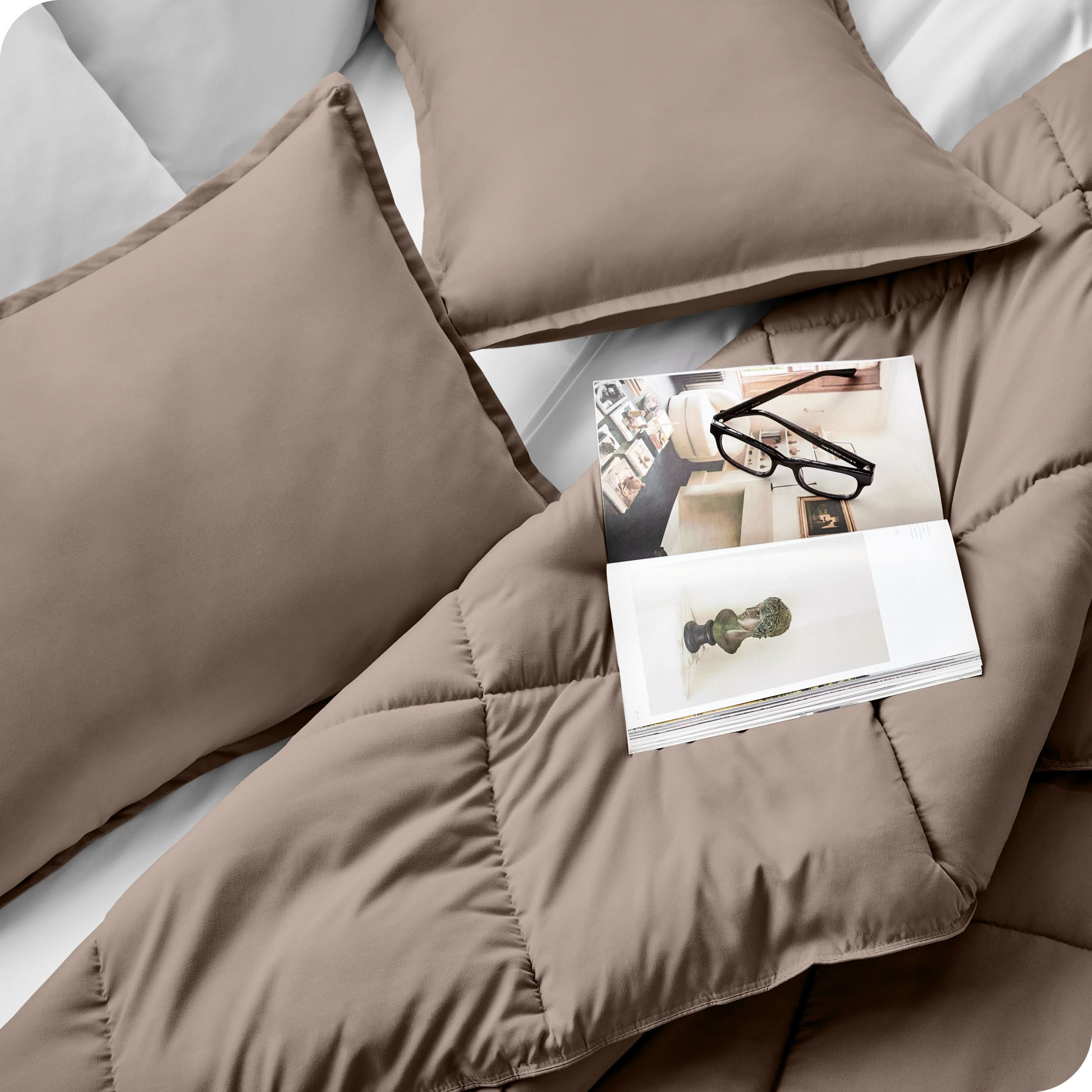 Close up of a comforter set on a bed. There are glasses and a magazine on top of the comforter.