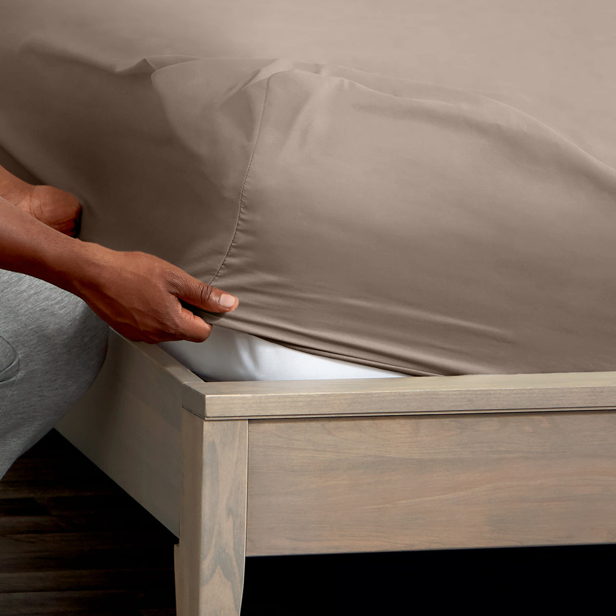 A man is putting a fitted sheet on a bed