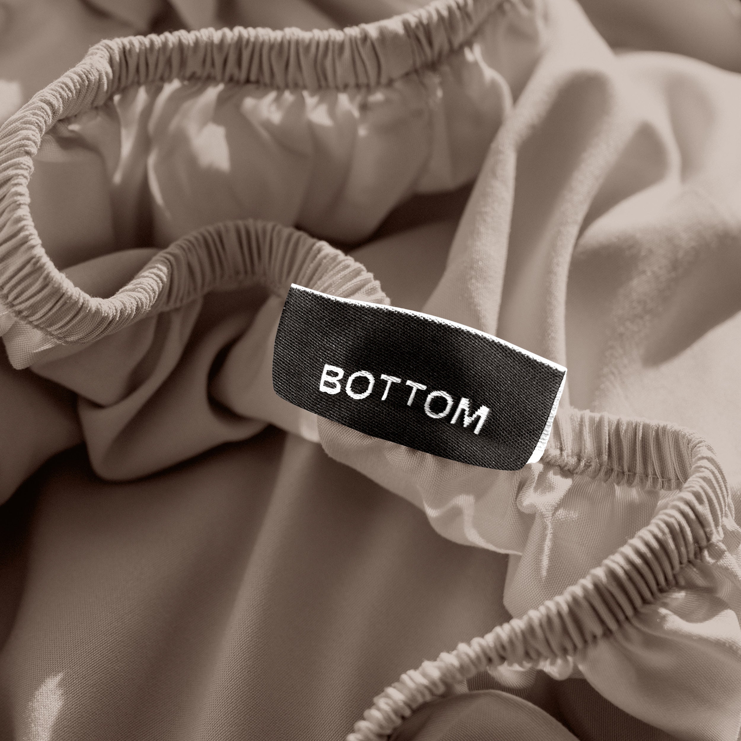A close-up of a fitted sheet with a label printed with the word 'BOTTOM' in white.