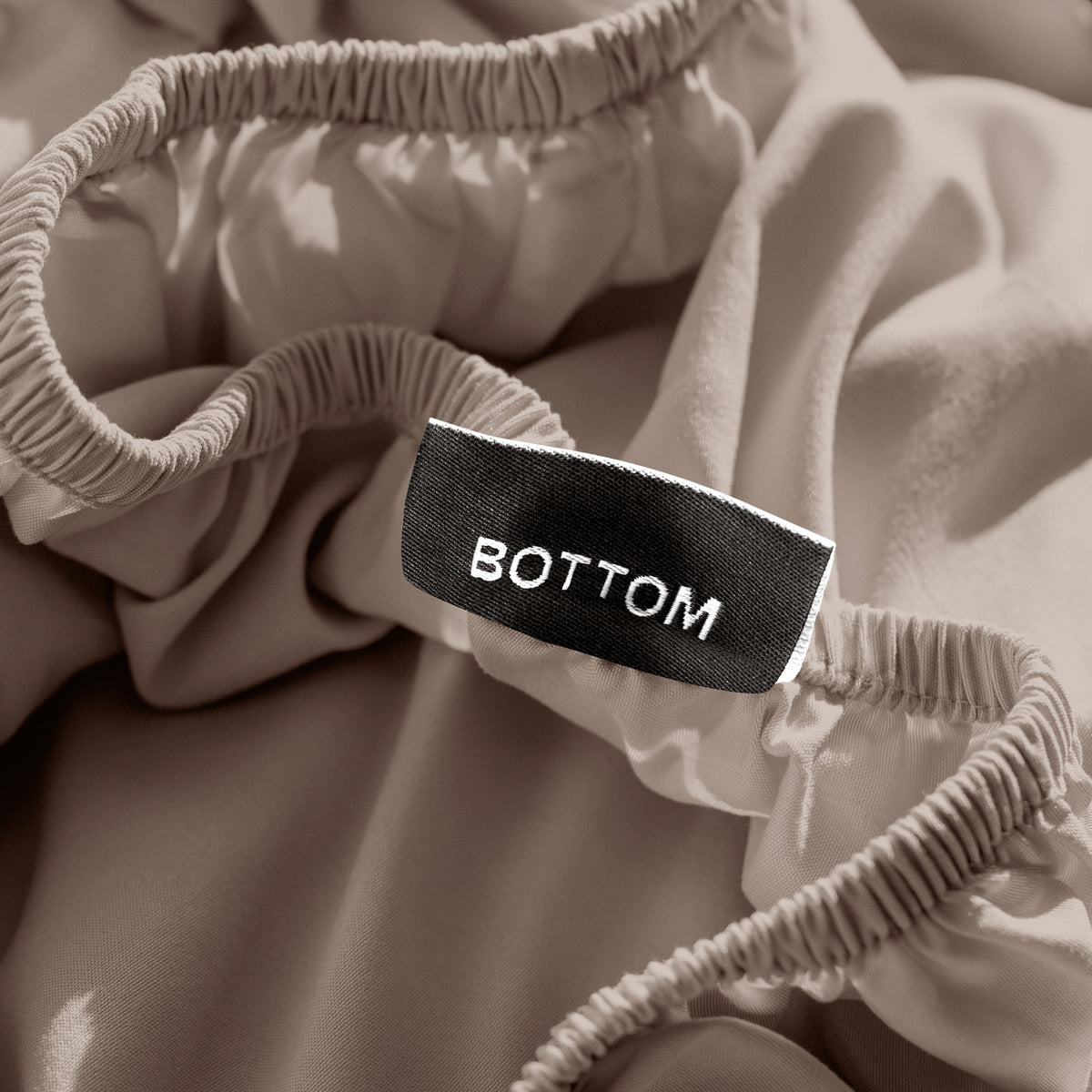 A close-up of a fitted sheet with a label printed with the word 'BOTTOM' in white.