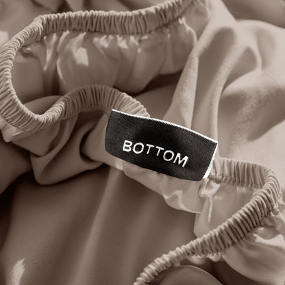 A close-up of a fitted sheet with a label printed with the word 'BOTTOM' in white.