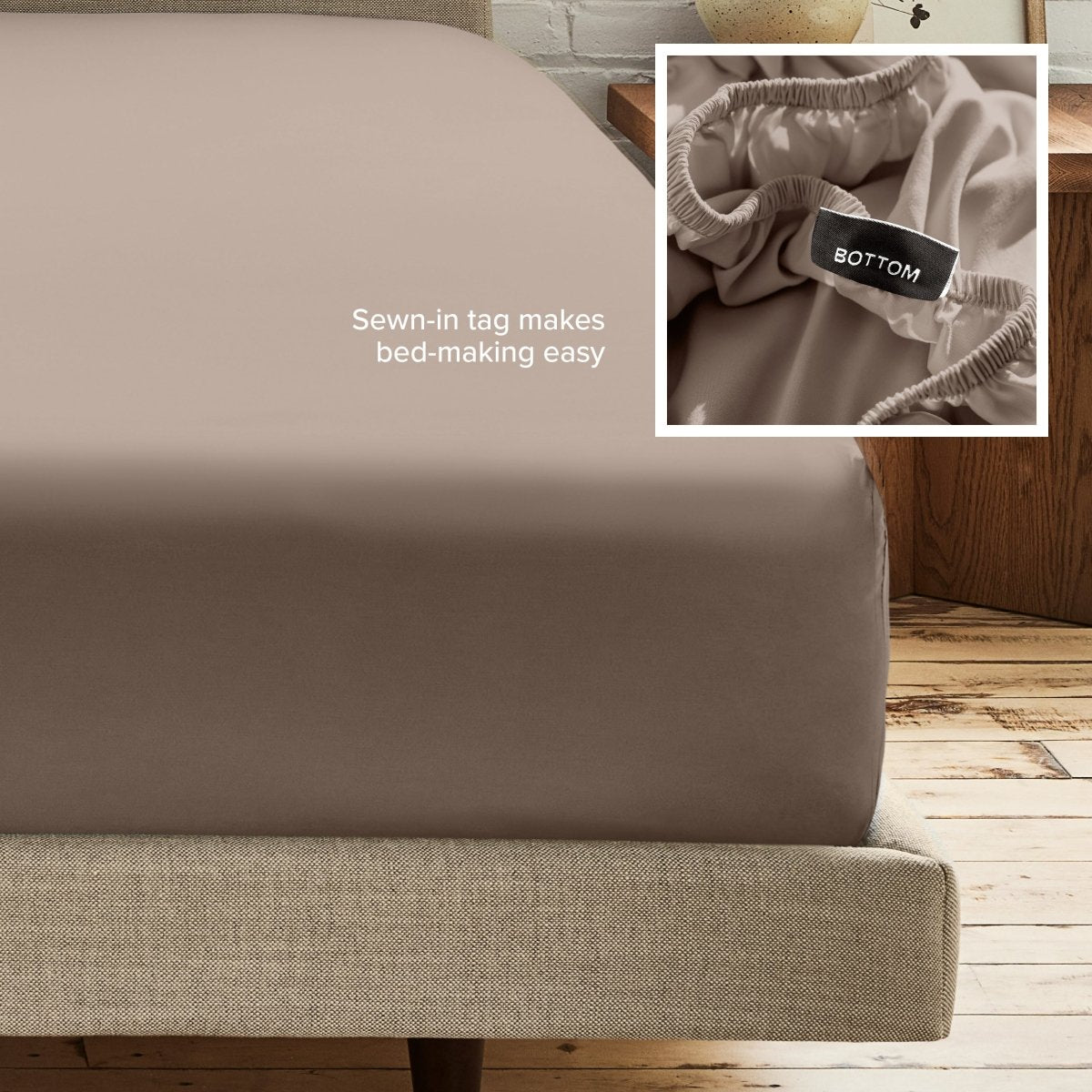 A fitted bed sheet on a bed frame with a small inset close-up of the elastic and a sewn-in tag labeled BOTTOM. White text on the sheet reads, 'Sewn-in tag makes bed-making easy.