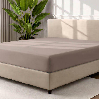 Man adjusting fitted sheet on a bed with white pillows.