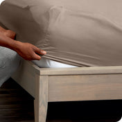 A man is putting a fitted sheet on a mattress