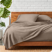 A wooden bed frame with a microfiber sheet set on the mattress.