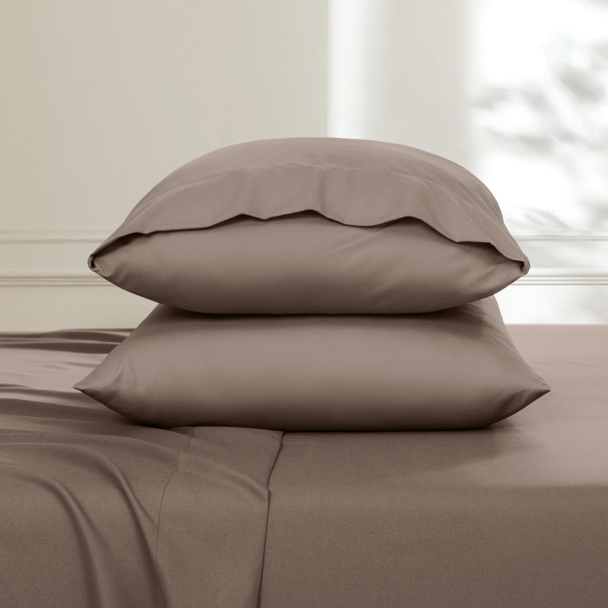 Two pillows stacked on a bed with a neutral background