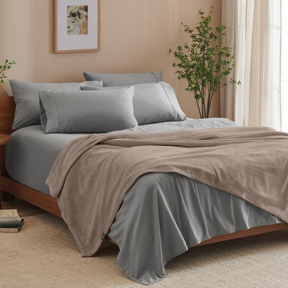 A bed made with grey sheets and a microplush blanket