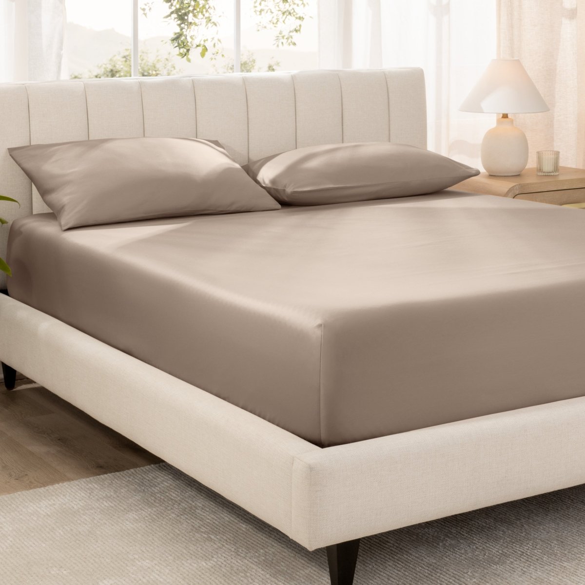 Bed with fitted sheet and pillowcases in a bright room.