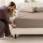 Woman adjusting a fitted sheet on a bed in a bedroom setting