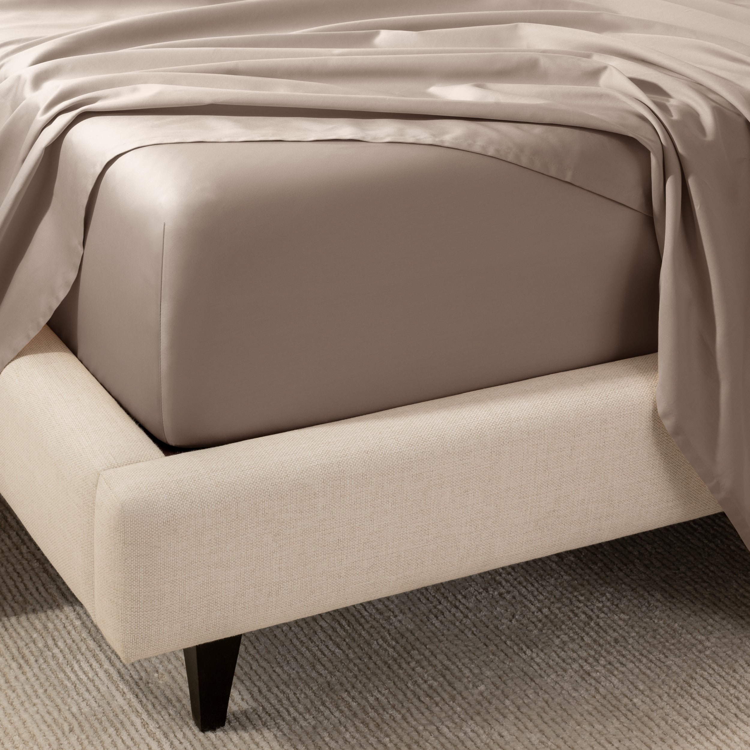 A close-up of the corner of a bed with a fitted sheet and matching flat sheet.