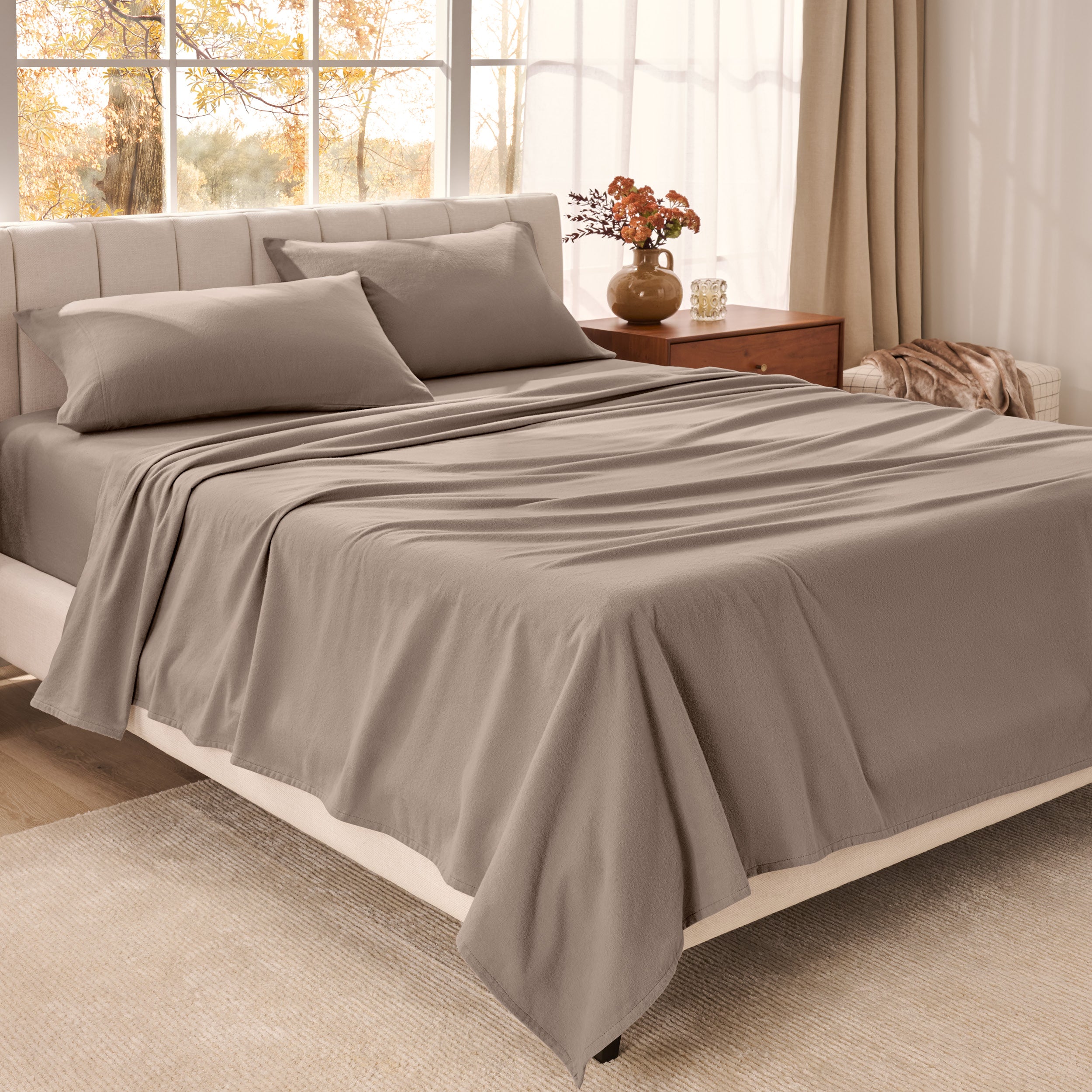 Bed sheets on a neatly made bed in a bright bedroom with large windows.