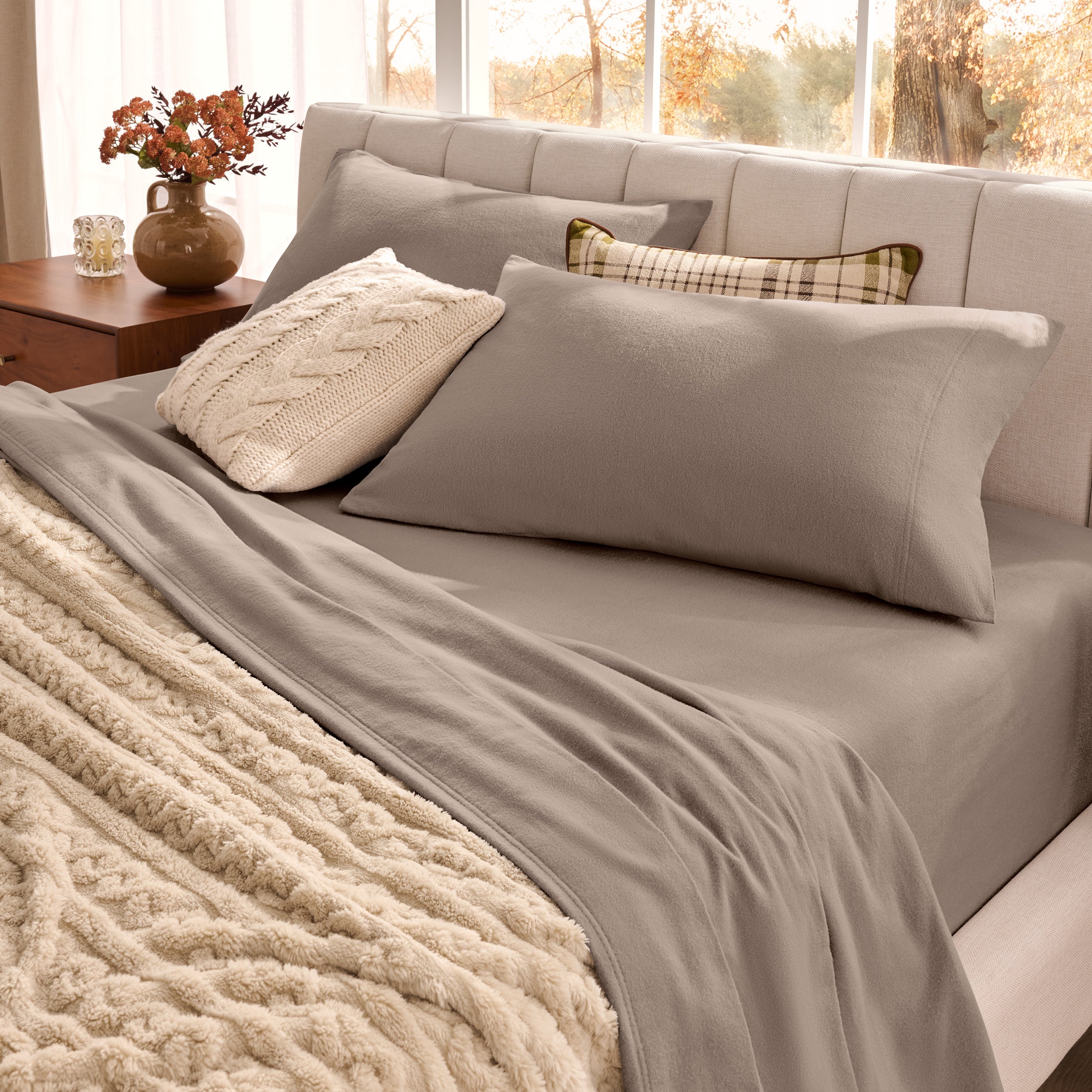 Neatly made bed with organic flannel sheets  and a beige blanket in a bright bedroom.