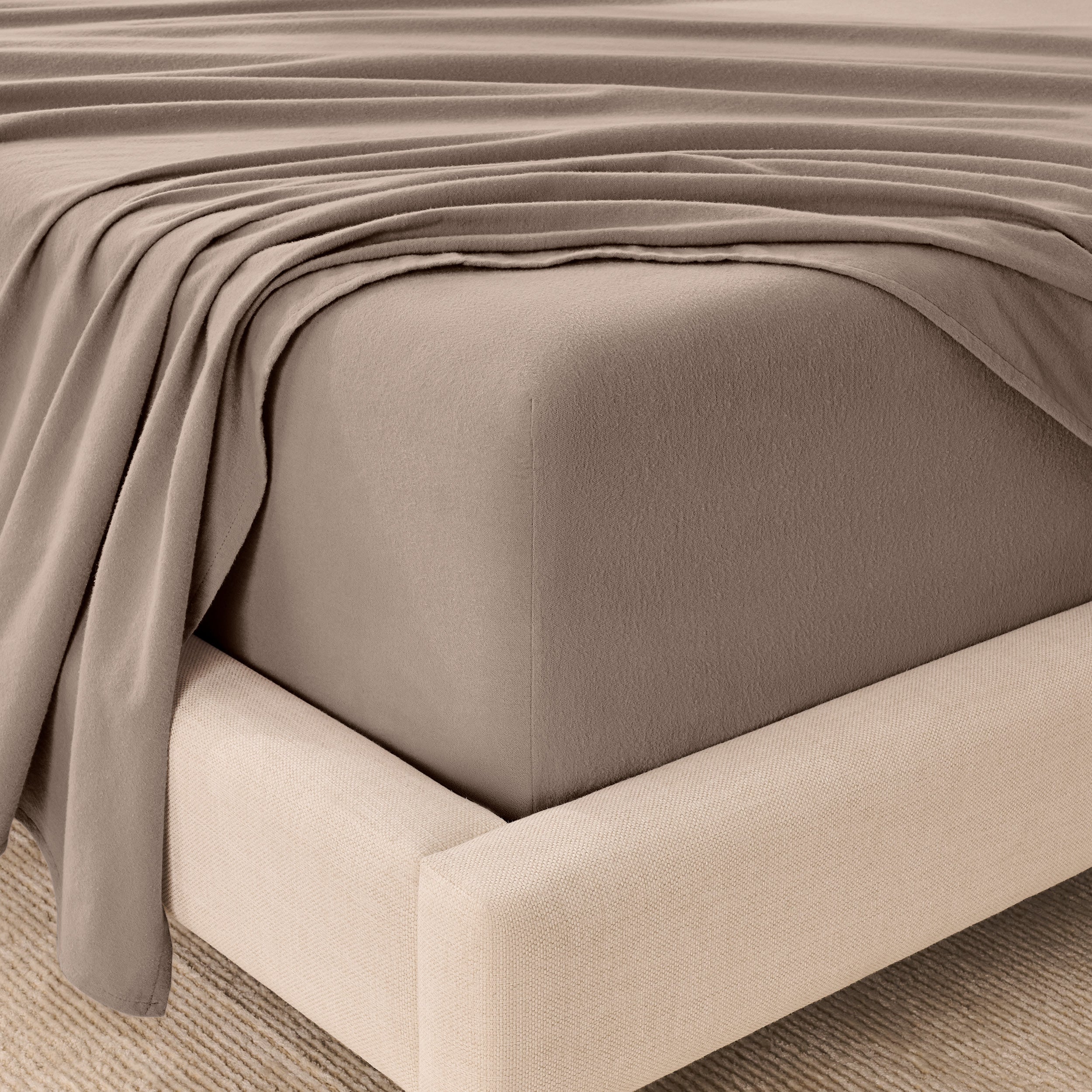 Fitted sheet and top sheet on a mattress with a beige bed frame