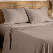 Organic jersey bed sheets and pillows on a bed with a wicker headboard.
