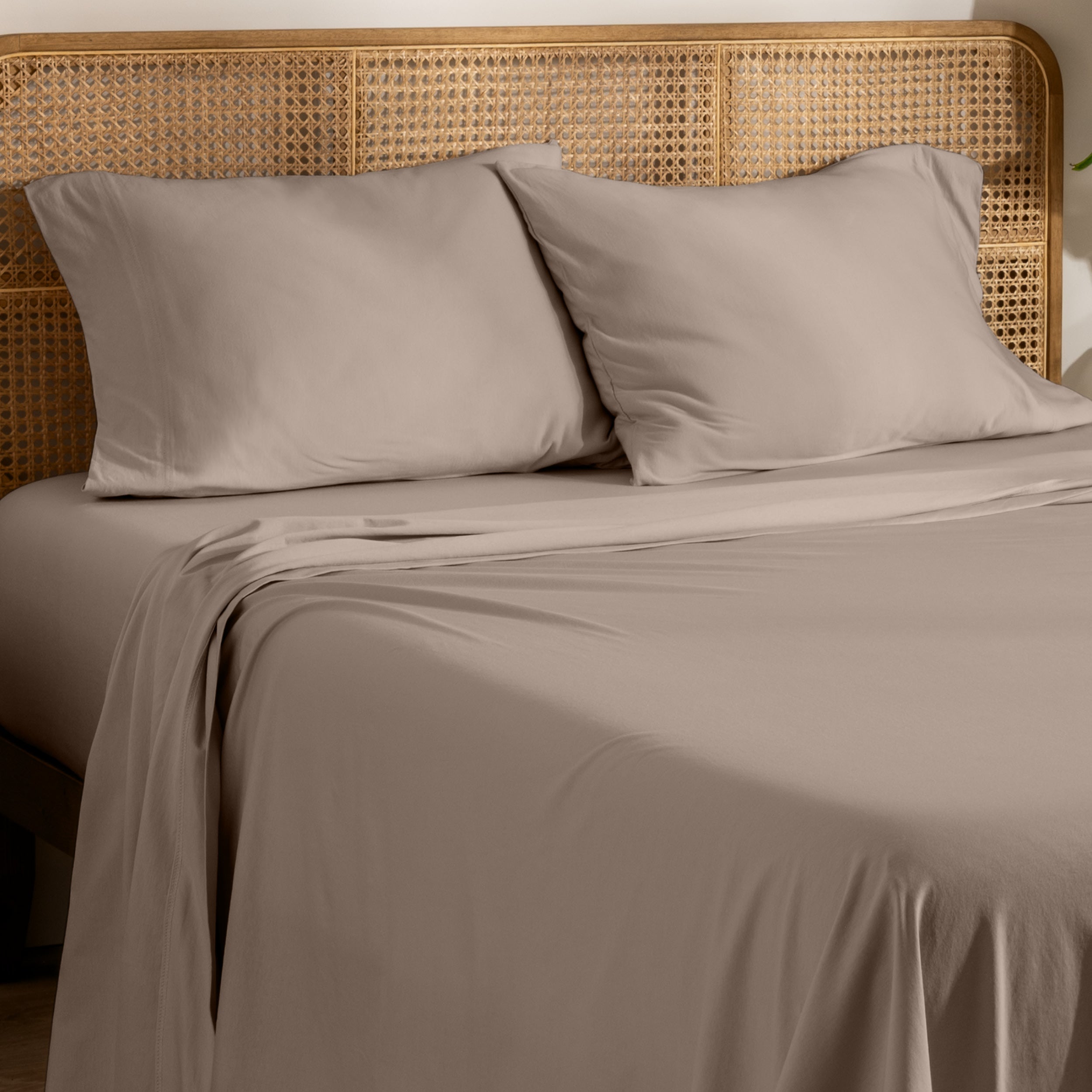 Organic jersey bed sheets and pillows on a bed with a wicker headboard.
