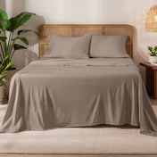 Organic cotton jersey sheets on a bed with a wicker headboard in a room with plants and a lamp.
