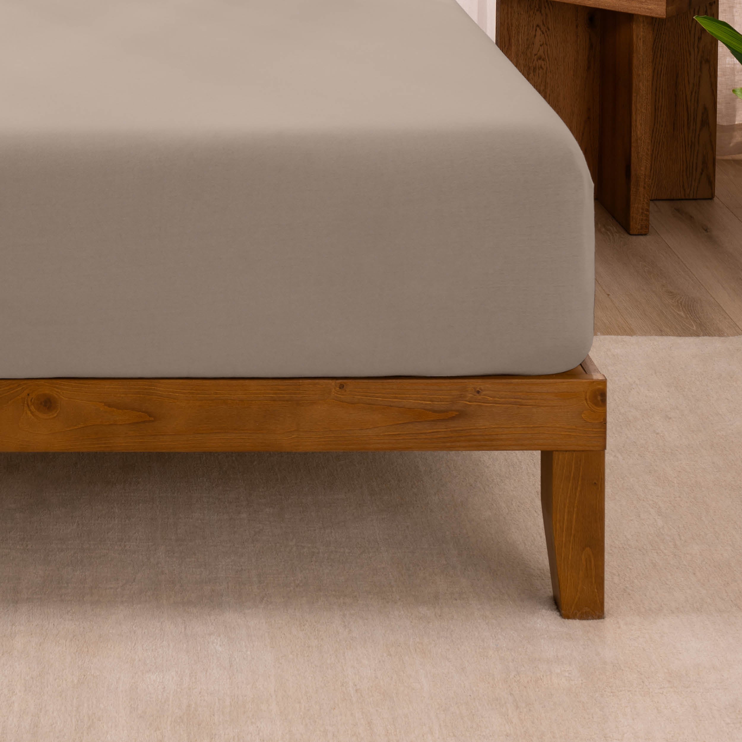 Fitted sheet on a wooden bed frame with a neutral background