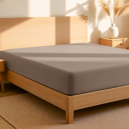 Fitted sheet on a bed in a bedroom setting with a lamp and plant.