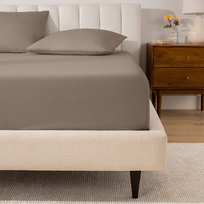 A percale fitted sheet and pillowcases on a bed in a bedroom with a wooden nightstand.
