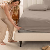 Woman in pajamas adjusting bed sheets on a bed.