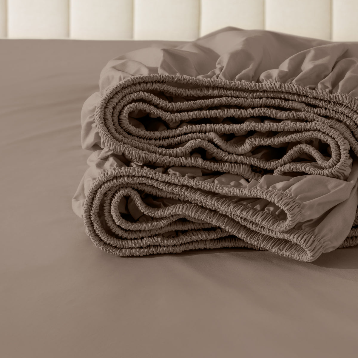 Folded fitted sheet on a bed with a neutral background