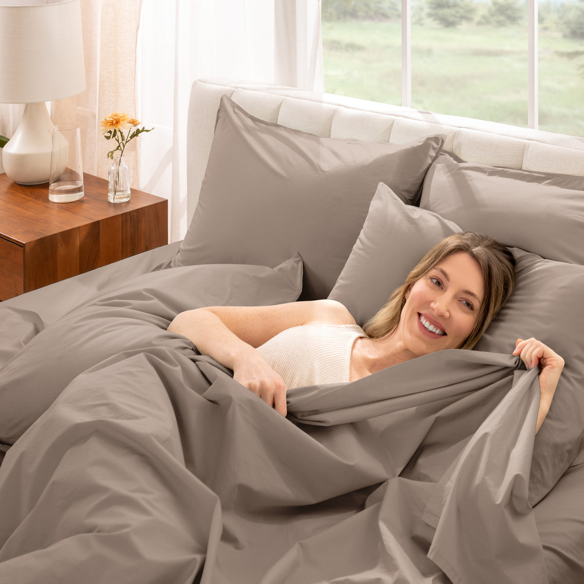Woman lying in bed with percale bedding in a bright bedroom