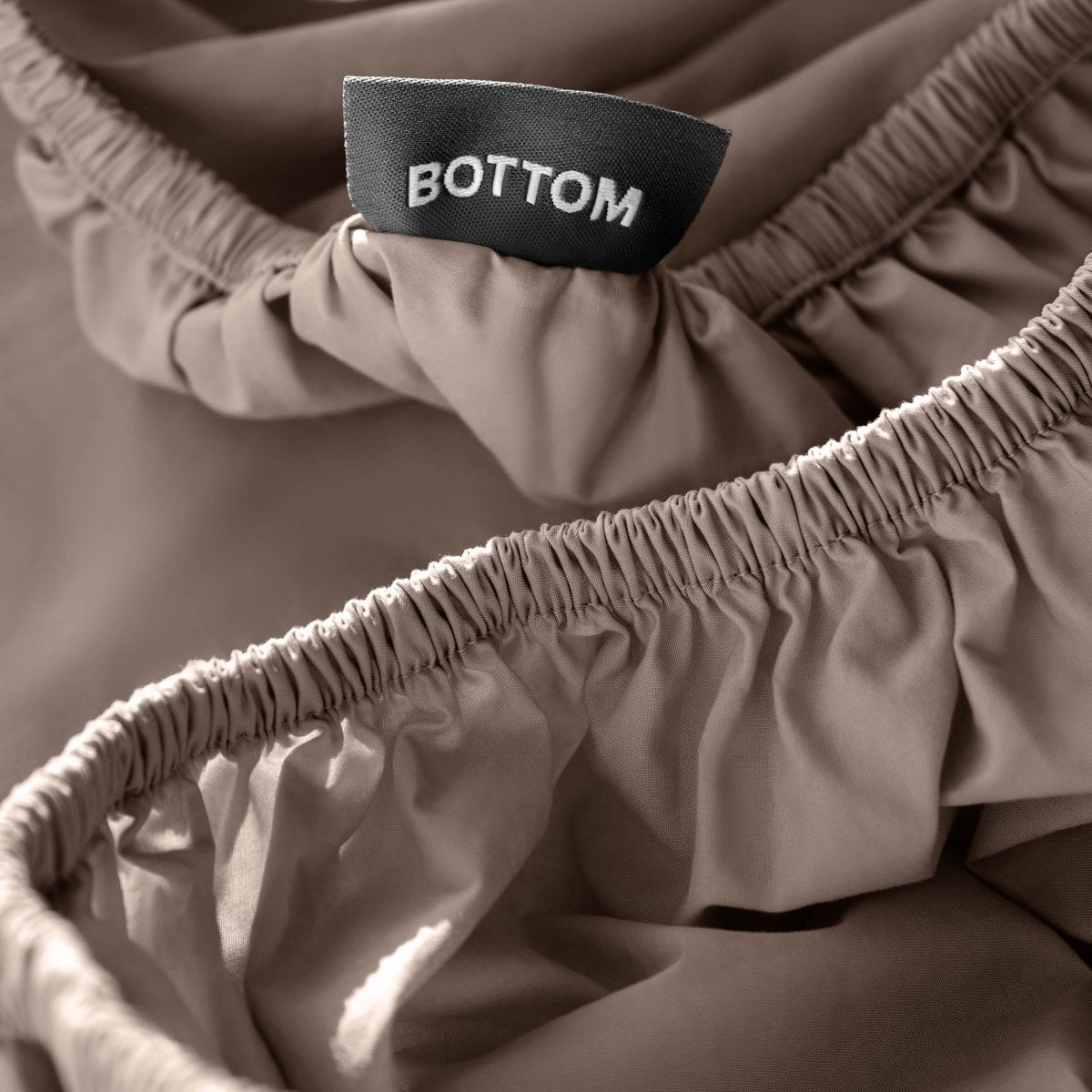 Close-up of a fitted sheet with a black fabric brand label reading BOTTOM.
