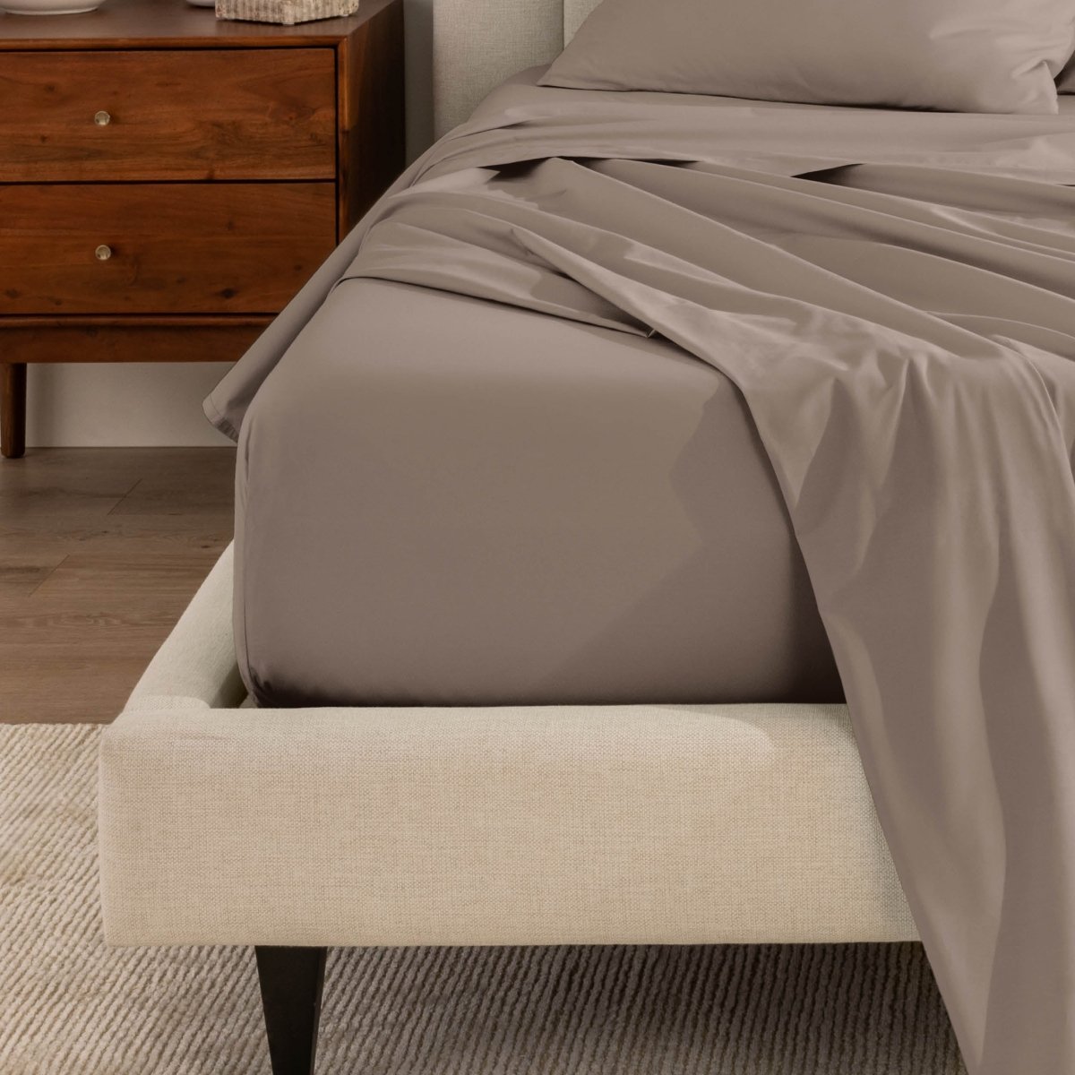 Top sheet and a matching fitted sheet on a bed with a beige bed frame