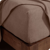 Corner of the bed with a fitted sheet on the mattress and a flat sheet draped over the side and end