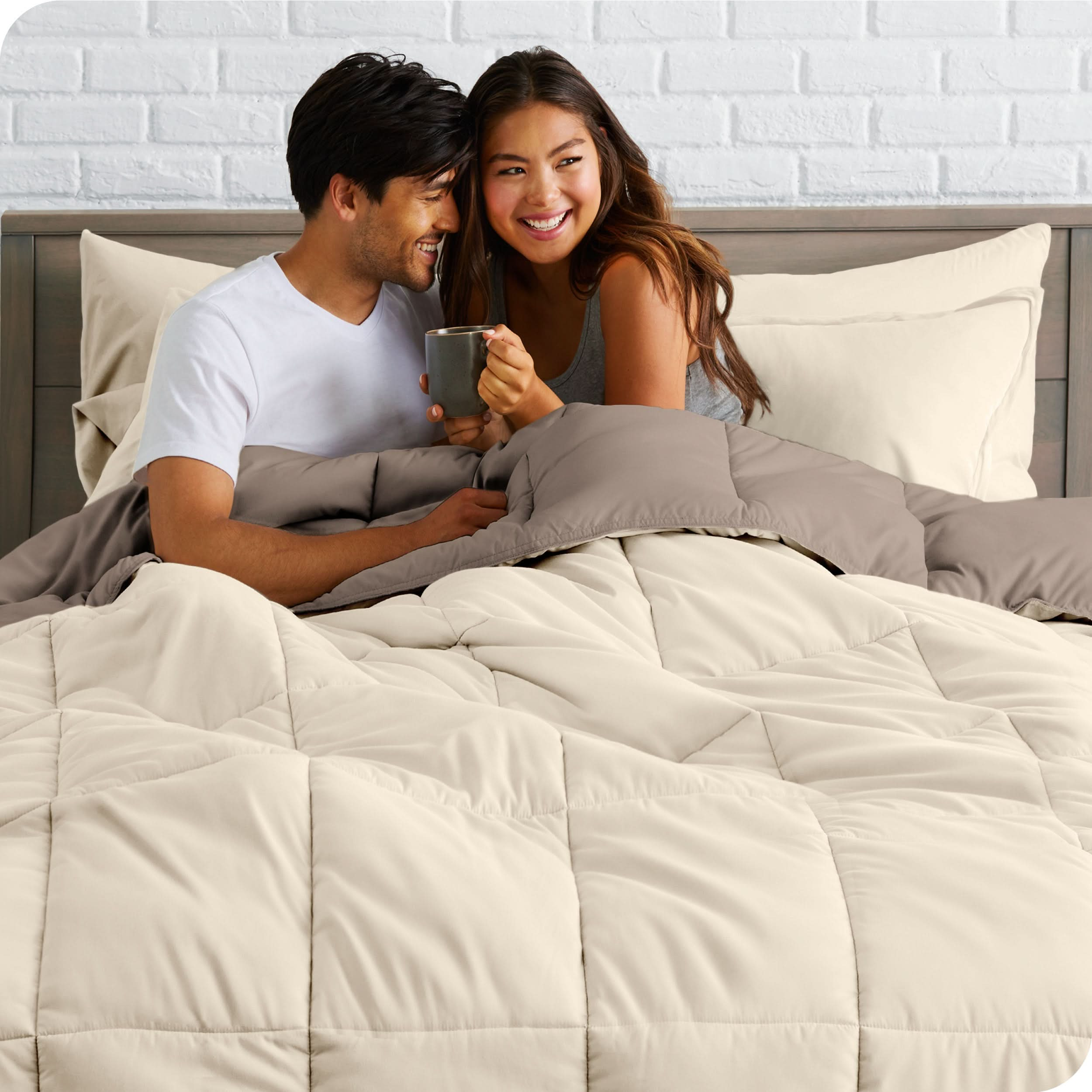 A couple sitting in a bed made with a reversible comforter and sheet set