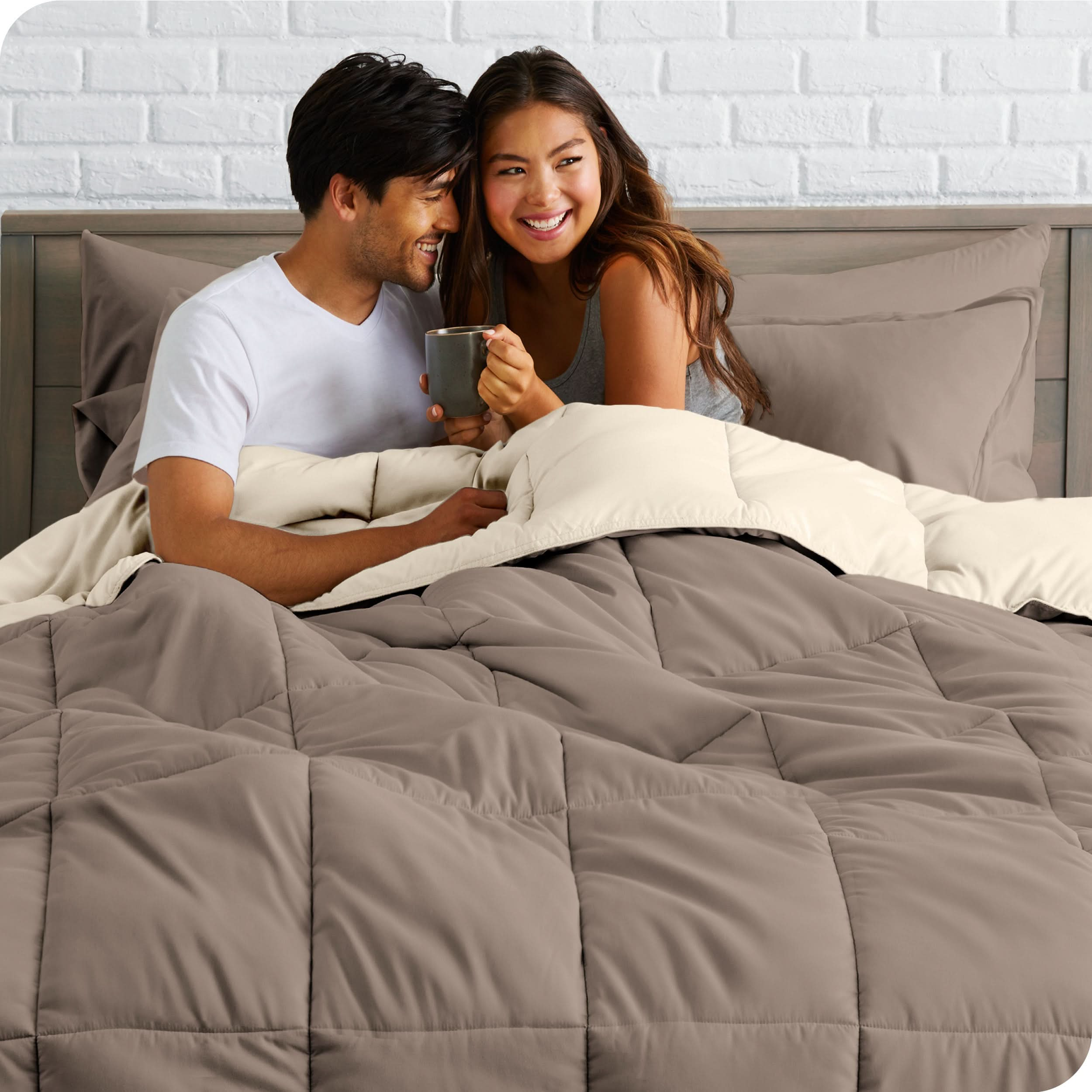 A couple sitting in a bed made with a reversible comforter and sheet set