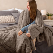 Fluffy blanket draped over a woman sitting on the end of a bed