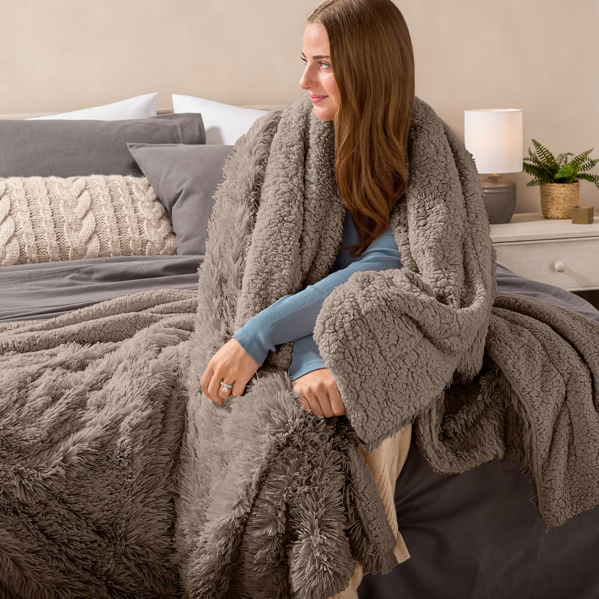 Fluffy blanket draped over a woman sitting on the end of a bed