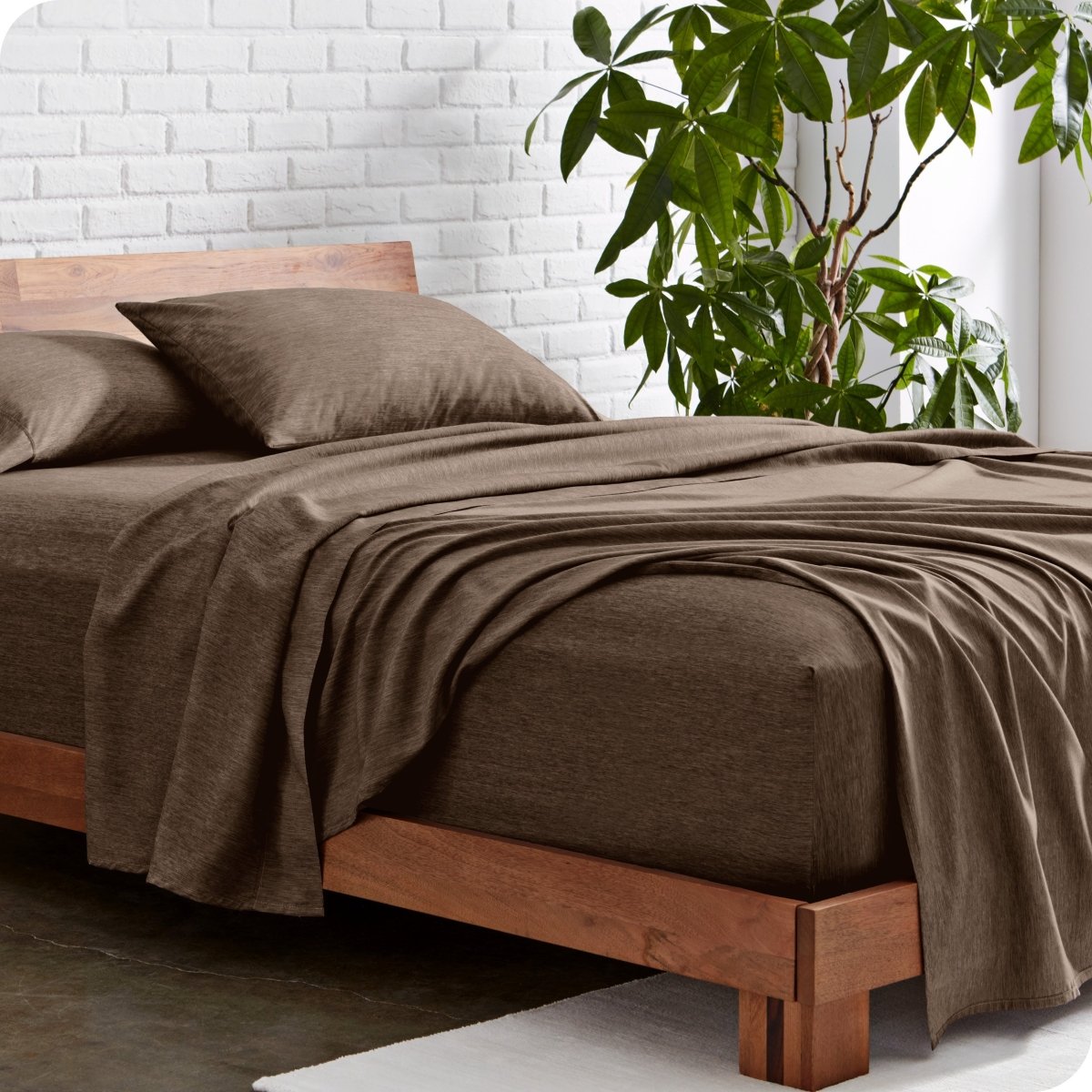 Bed with heather sheets and wooden frame against a white brick wall with a plant.