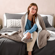 A woman sitting on a bed with a Sherpa blanket around her
