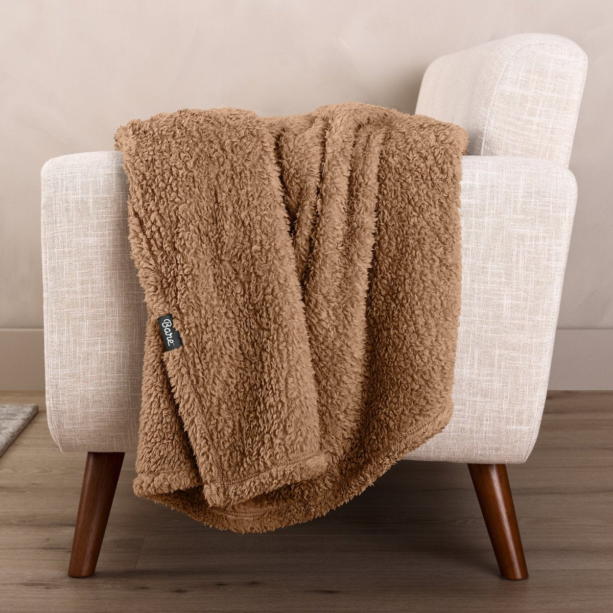 Faux shearling blanket draped over a beige armchair with a wooden base.